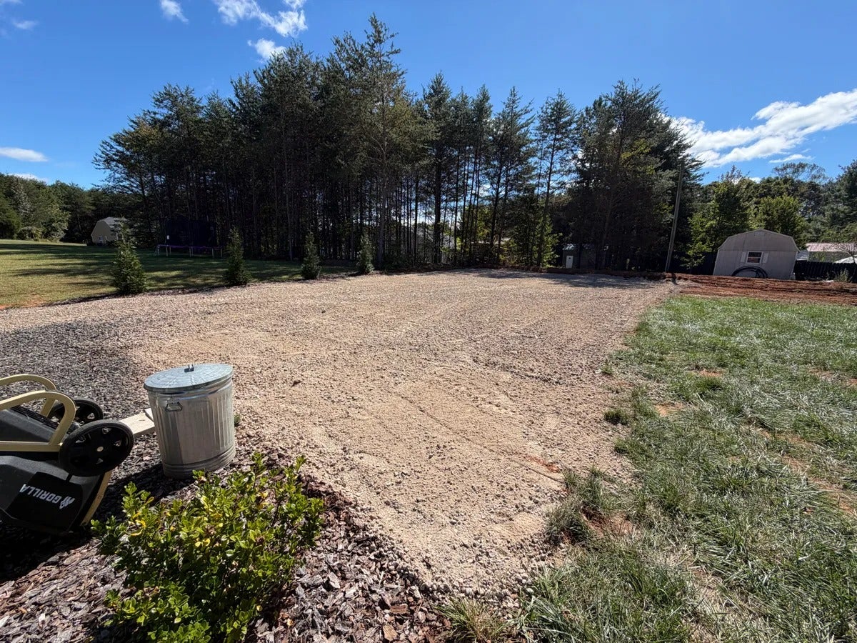 A wide, level gravel driveway next to a grassy area, bordered by evergreen trees