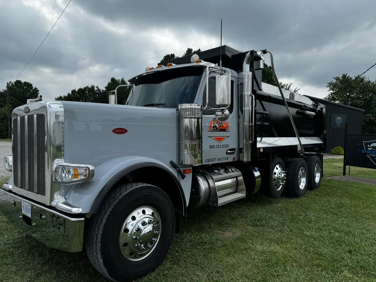 A Peterbilt dump truck with a black bed, chrome grille, and chrome accents parked on grass.
