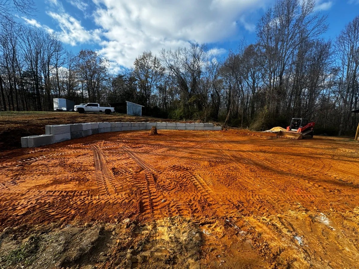 Excavated construction site with red dirt, a concrete block retaining wall, and a track loader.